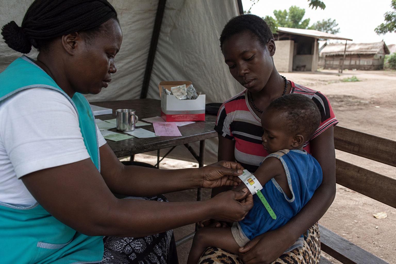 Nurse measuring a toddler's arm at a rural nutrition screening tent